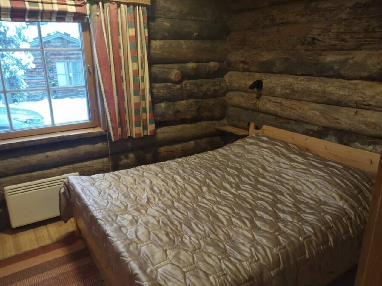 A log cabin room with a bed, a window with curtains, and a radiator.