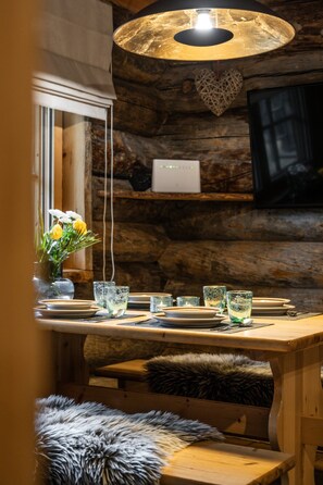 Ein rustikales Holzinterieur mit einem Esstisch, gedeckt für vier Personen, einer Blumenvase und einer hängenden Lampe.