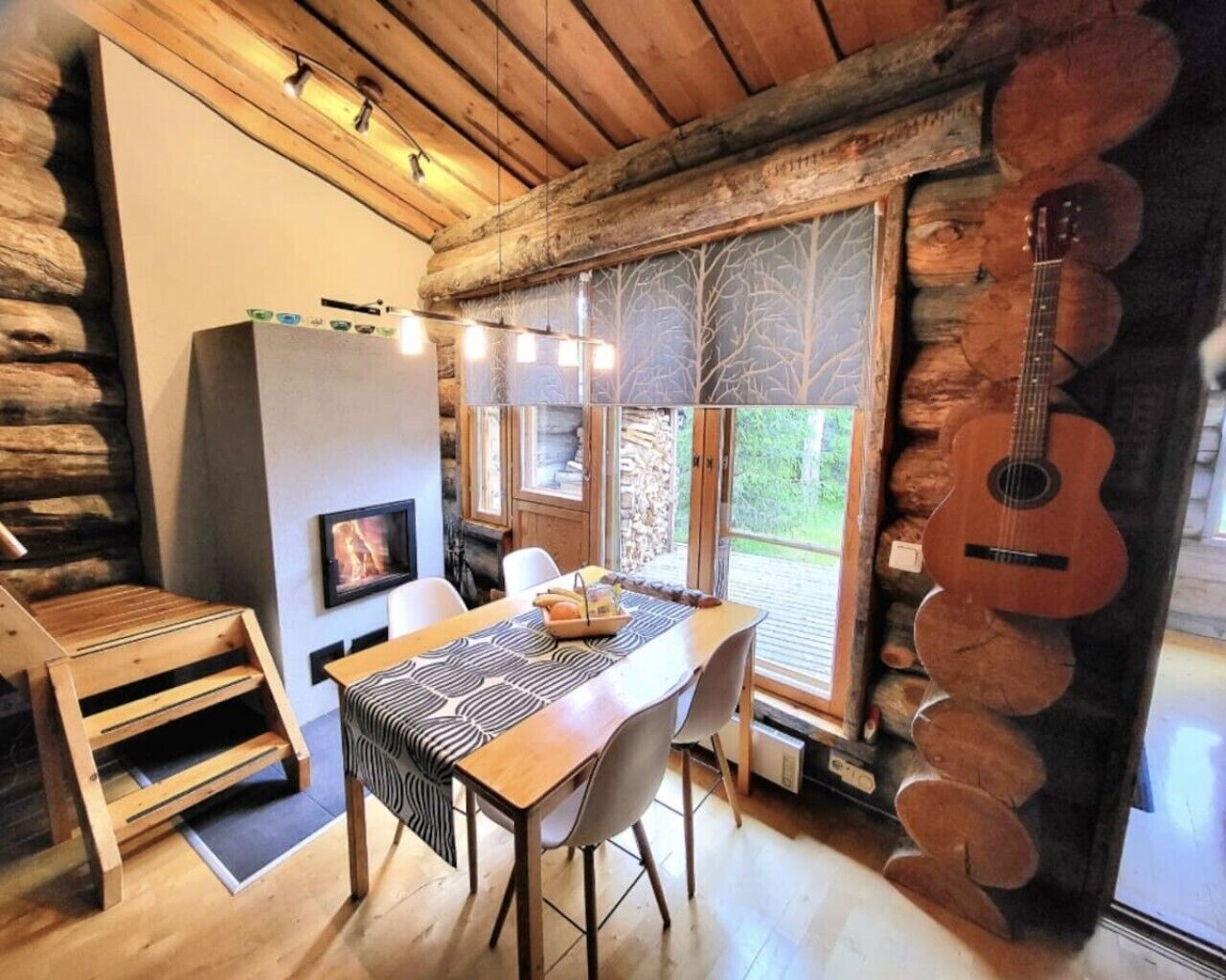 A rustic cabin interior with a dining table, chairs, a fireplace, and a guitar.