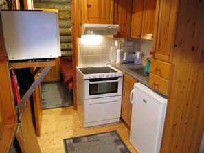Eine kleine Küche mit Holzschränken, einem Einbauofen, einem Kühlschrank und einer Mikrowelle.
