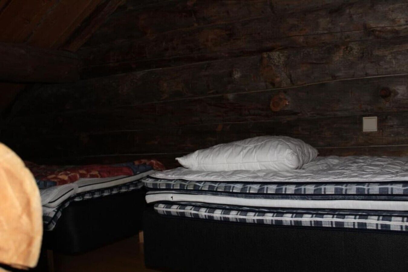 Una habitación pequeña y con poca luz, con dos camas, una con almohada blanca y otra con manta estampada.