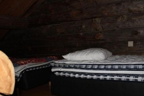 A small, dimly lit room with two beds, one with a white pillow and the other with a patterned blanket. - Saukkolampi 1 | Traditional Log Apt with Sauna (Ruka)