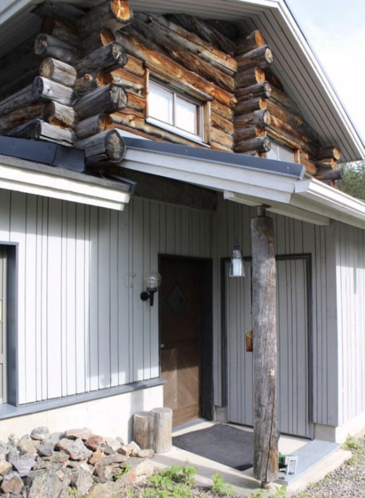 A log cabin with a front porch, a door, and a small stone wall.