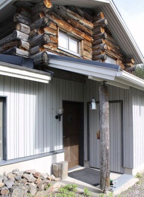 A log cabin with a front porch, a door, and a small stone wall. - Rukaköngäs D 17 | Comfy Apt with Fireplace & Sauna (Ruka)