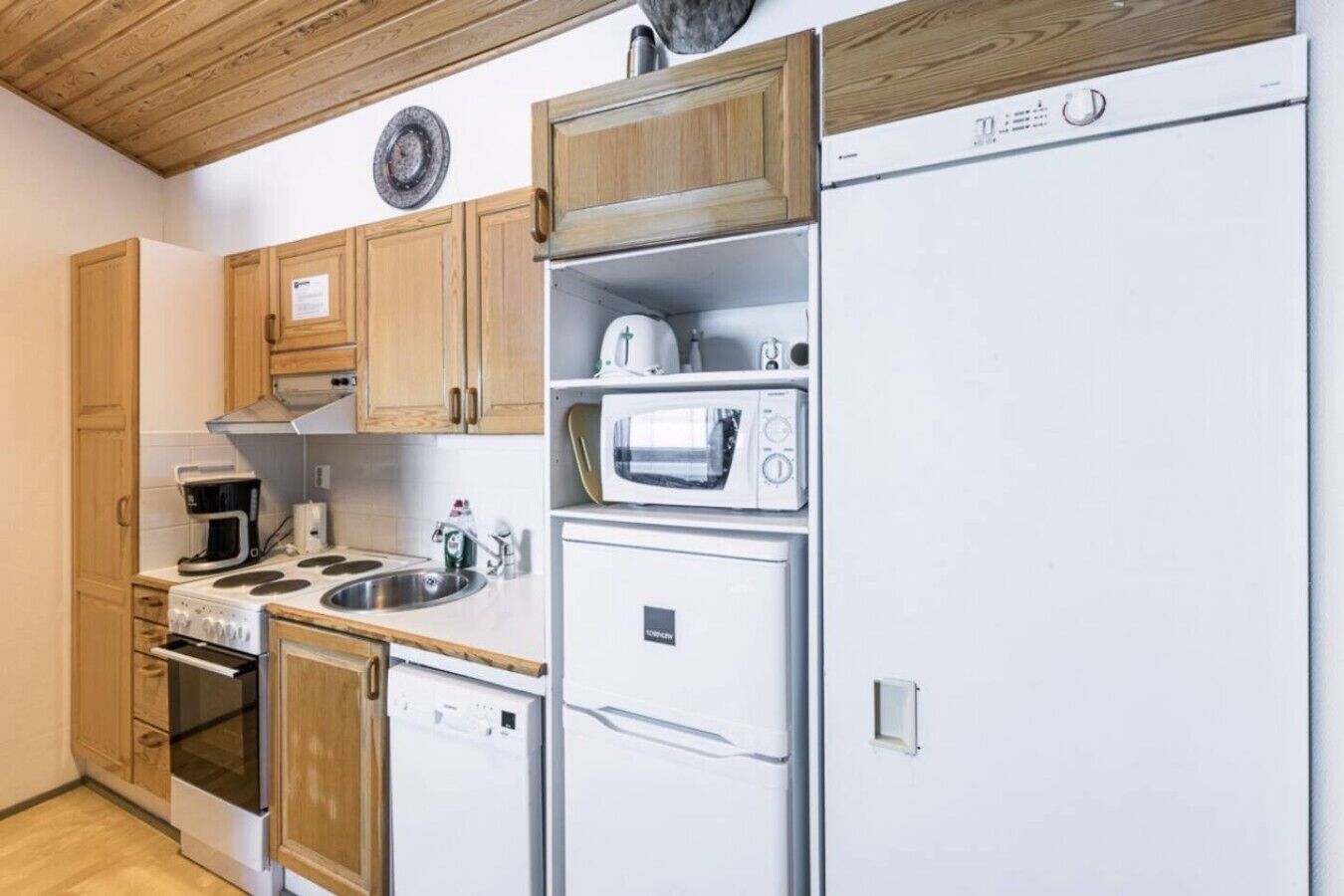 A compact kitchen with a stove, microwave, dishwasher, and wooden cabinets.