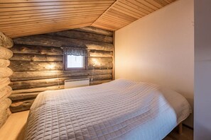 A cozy log cabin bedroom with a bed, a window with a curtain, and a wooden ceiling. - Rukaköngäs D 17 | Comfy Apt with Fireplace & Sauna (Ruka)
