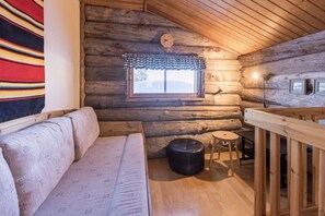 A log cabin interior with a sofa, a small stool, a window with a checkered valance, and a wooden railing. - Rukaköngäs D 17 | Comfy Apt with Fireplace & Sauna (Ruka)