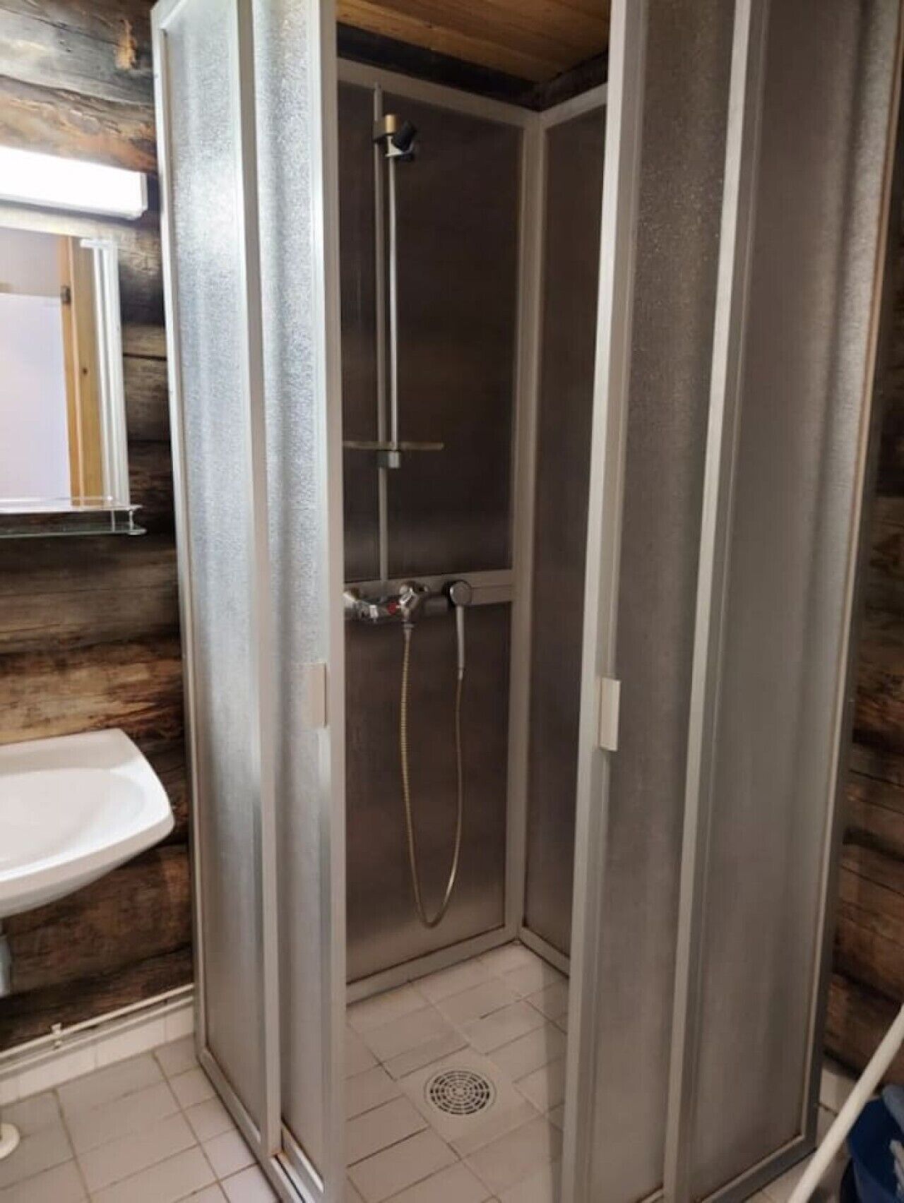 A bathroom with a shower enclosure, a sink, and a wooden wall.