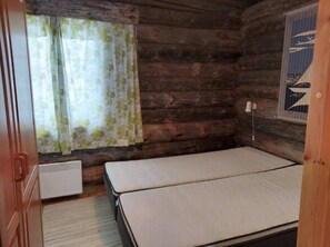 A cabin room with a bed, a window with curtains, a radiator, and a wall-mounted light fixture. - Rukan Kuukkeli B15 | Comfy Apt Near Ski Lifts (Ruka)