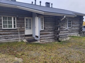 Een vakantiehuisje van hout met een voordeur, een klein terras en een schoorsteen.