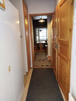 En smal hall med trädörrar på vardera sidan, som leder in till ett rum med ett fönster och ett bord.