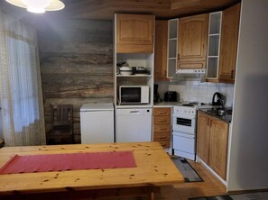 A compact kitchen with wooden cabinets, a microwave, a small refrigerator, and a stove. - Rukan Kuukkeli B15 | Comfy Apt Near Ski Lifts (Ruka)