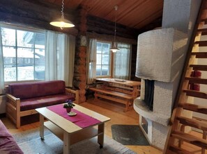 Een knus houten interieur met een slaapbank, een tafel met een vaas, een bankje, een open haard en grote ramen.