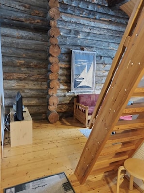 A cabin interior with a wooden floor, a bed with a headboard, a wooden ladder, a wall-mounted shelf, and a framed picture. - Rukan Kuukkeli B15 | Comfy Apt Near Ski Lifts (Ruka)