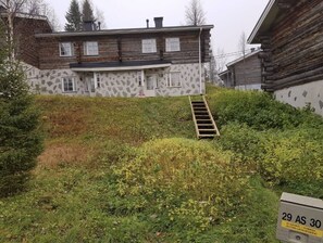 A log cabin with a stone facade, a wooden staircase, and a grassy yard. - Rukan Kuukkeli D30 | Spacious 3BR Apt for 8 (Ruka)