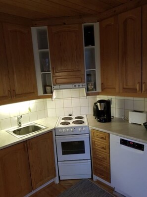 A kitchen with wooden cabinets, a white stove, a sink, and a coffee maker. - Rukan Kuukkeli D30 | Spacious 3BR Apt for 8 (Ruka)