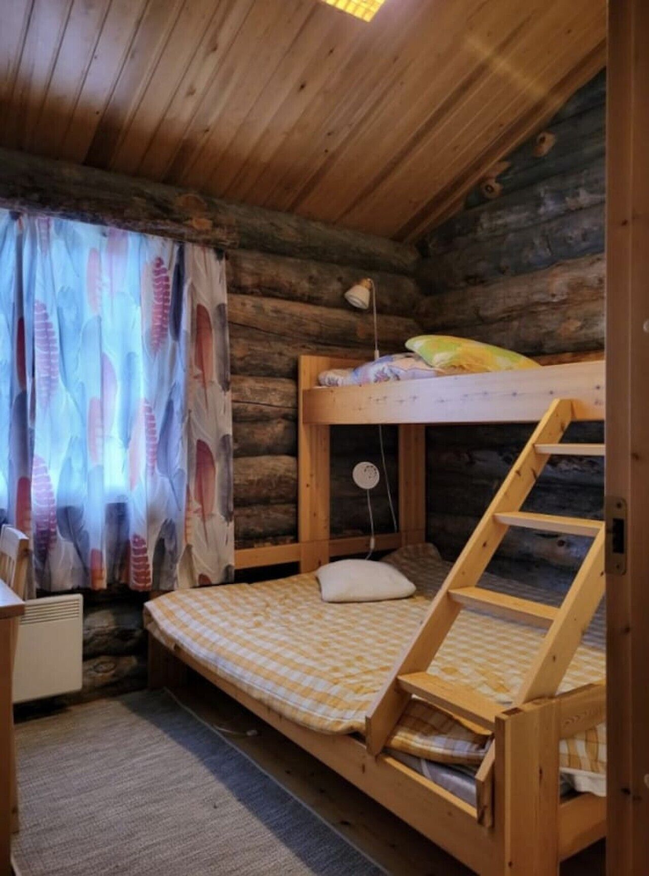A cabin with a bunk bed, a desk, and a window with curtains.