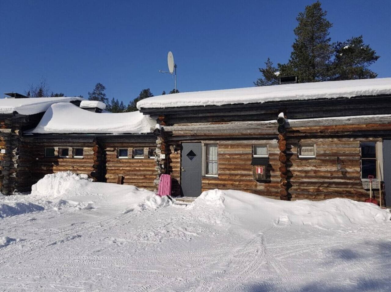 A log cabin with a snow-covered roof and a satellite dish.