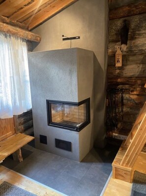 L’intérieur d’une cabane en rondins, avec une cheminée en pierre, des bancs en bois et une esthétique rustique.