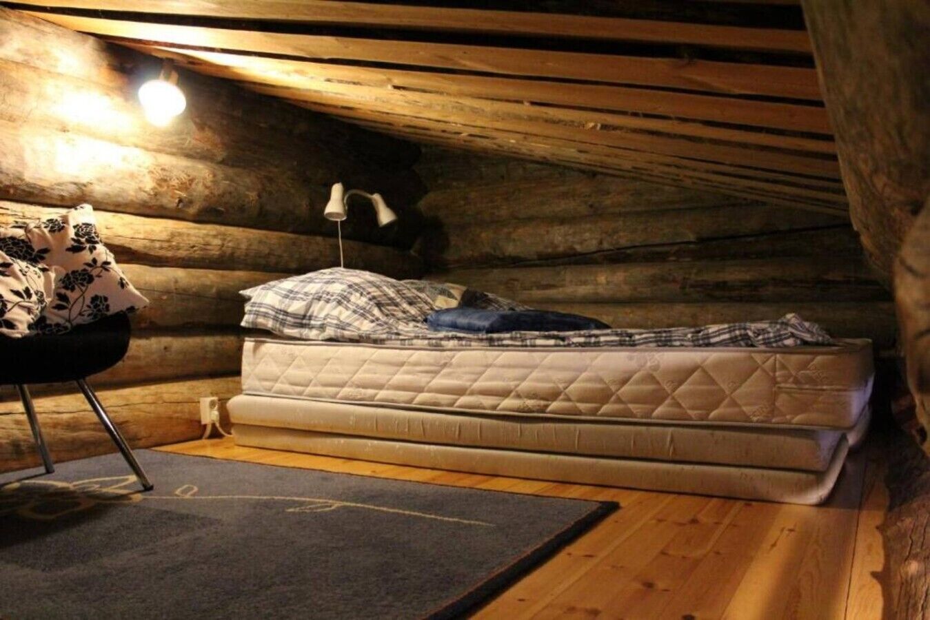 A cozy attic bedroom with a single mattress, a lamp, and a chair.