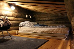 Une chambre mansardée chaleureuse, avec un matelas simple, une lampe et une chaise.