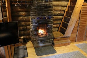 Une cheminée en pierre, avec un téléviseur placé à gauche, des marches en bois menant à une mezzanine, et une porte en bois à droite.