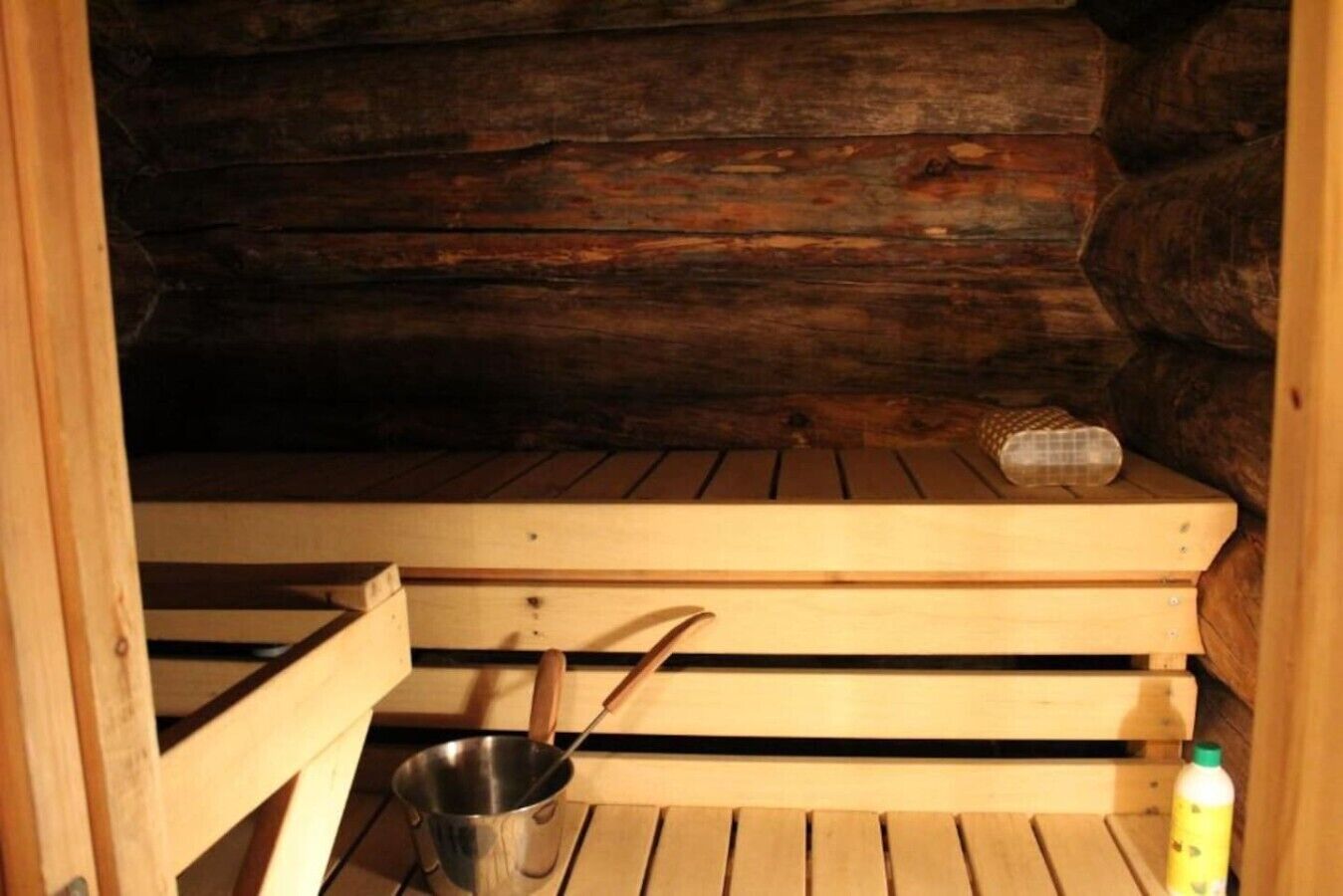 Un sauna avec des bancs en bois, un récipient en métal et une bouteille.