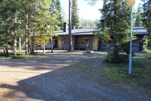 A rustic cabin with a gravel driveway, surrounded by trees.