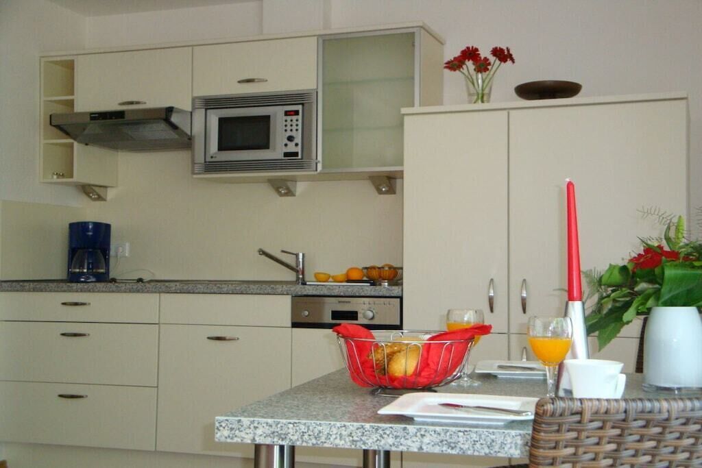 A kitchen with a microwave, sink, and a table with a basket of oranges and a red-handled brush.