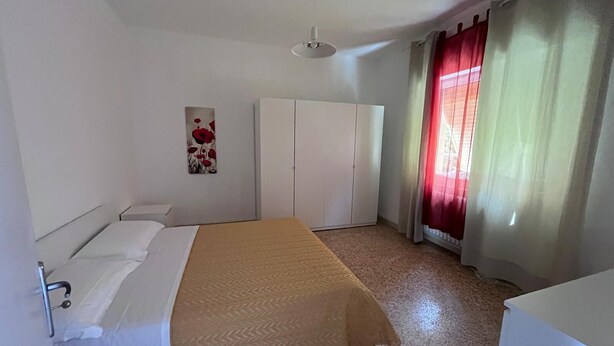 Quarto com cama, guarda-roupa, um quadro e janela com cortinas.
