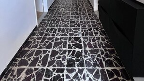 Corredor com piso estampado, paredes brancas e um móvel preto à direita.