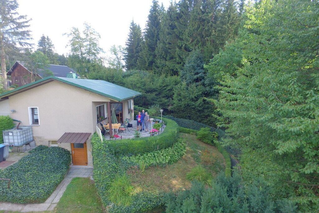 Een huis met een groen dak, een terras met tuinmeubilair en een tuin met verschillende planten en bomen.