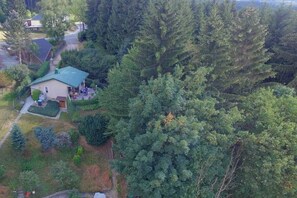 Uma casa cercada por uma floresta densa, com uma entrada de garagem visível e uma pequena varanda.