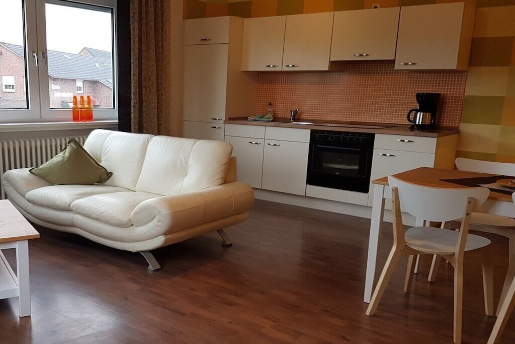 Eine moderne Küche mit weißen Schränken, einem schwarzen Backofen und einem Holzesstisch mit zwei Stühlen.