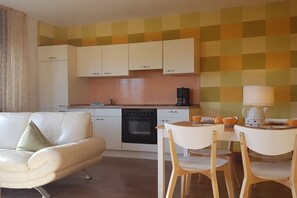 Eine kompakte Küche mit weißen Schränken, einer Kaffeemaschine und einem Essbereich mit Tisch und Stühlen.