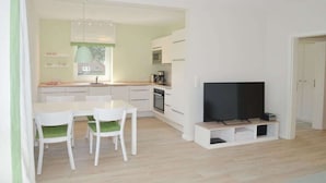 Espaço de estar moderno com área de jantar, kitchenette e televisão de ecrã plano.