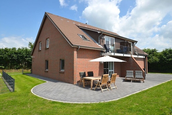 Une maison à deux étages avec une façade en briques, un balcon et un patio aménagé avec une table et des chaises.