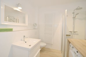 Une salle de bain avec un lavabo blanc, un miroir, des toilettes et une douche.