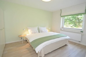 Une chambre à coucher avec un lit, une table de chevet, une lampe et une fenêtre donnant sur un paysage verdoyant.