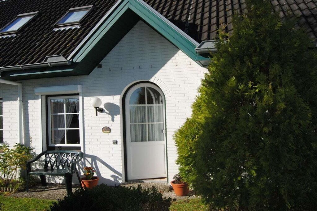 A white house with a green roof, a door with a window, and a bench outside.