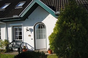 Een wit huis met een groen dak, een deur met een raam en een bank voor buiten.