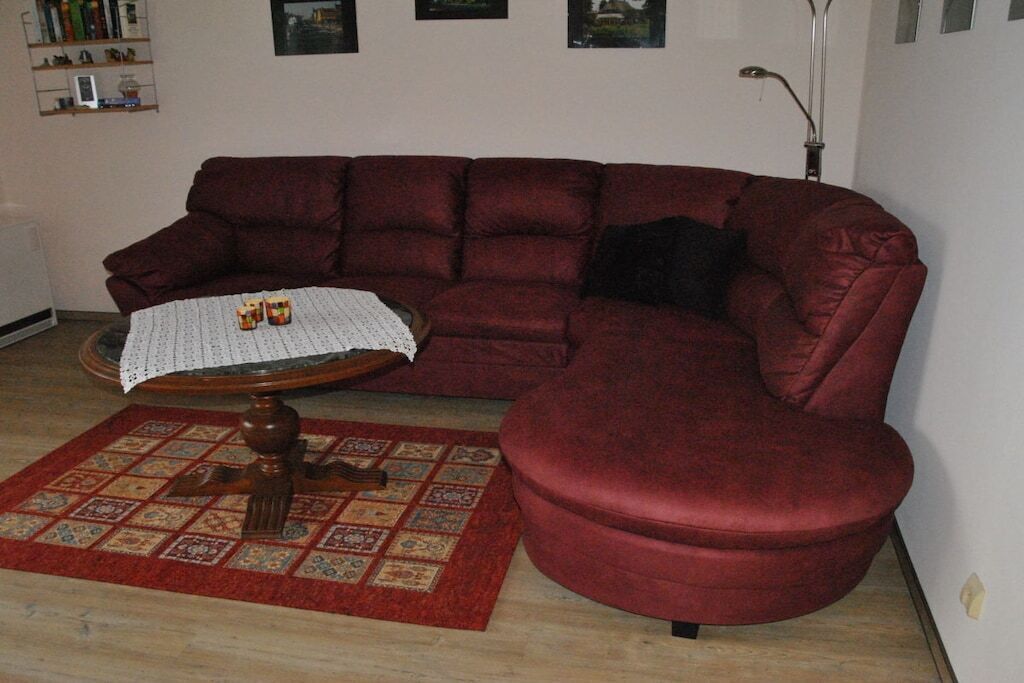 Een woonkamer met een rode bank, een kleine ronde tafel met een witte tafelkleed en een kamerbreed tapijt met een patroon.