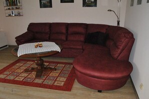 A living room with a red sofa, a small round table with a white tablecloth, and a patterned rug. - Holiday apartment with 2 bedrooms (Friedrichskoog)