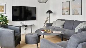 A modern living room with a grey sofa, a round coffee table, and a flat-screen TV mounted on the wall. - VillaVilla 1000 - Ålbæk, Nordjylland (Ålbæk)