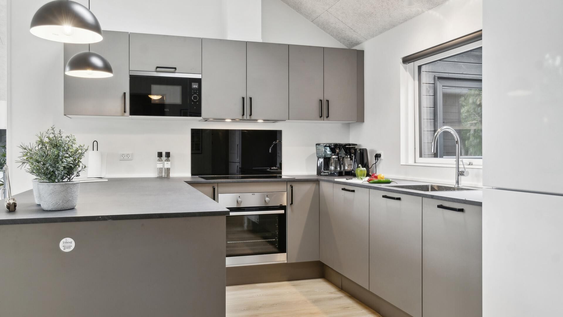 A modern kitchen with grey cabinets, a built-in oven, a microwave, and a coffee maker.