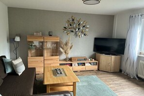 Un salon comprenant un canapé, une table basse, un téléviseur, des meubles en bois et un élément décoratif mural.
