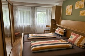 Une chambre avec deux lits, une chaise, une petite table et une fenêtre avec des rideaux légers.
