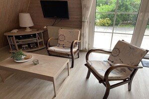 A cozy room with a wooden floor, a television mounted on the wall, a table with a lamp, and two chairs with nautical-themed upholstery. - Holiday home with 2 bedrooms (Spieka-Neufeld (Wurster Nordseeküste))