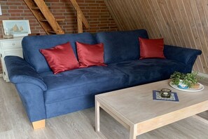 A blue sofa with red cushions, a wooden coffee table, and a small plant on a white side table. - Holiday home with 2 bedrooms (Spieka-Neufeld (Wurster Nordseeküste))