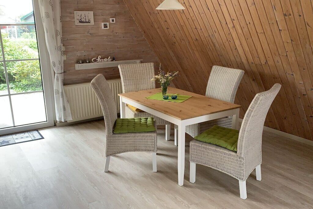 Un coin repas avec une table en bois et des chaises en osier, un radiateur et une vue par la fenêtre.